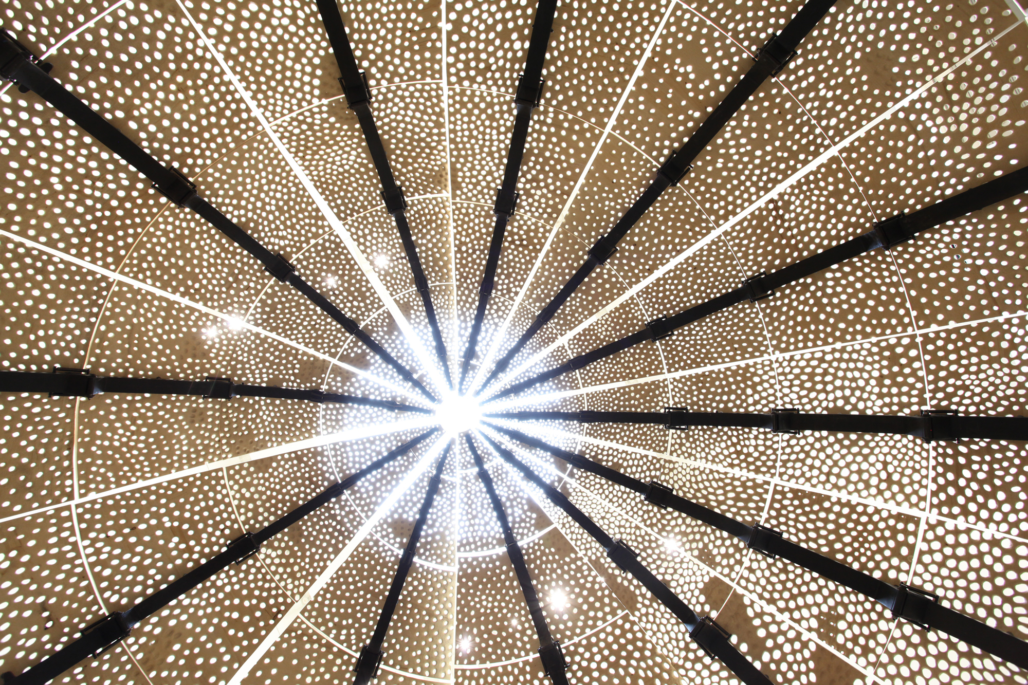Photograph from the inside of sculpture, triangular pieces with lace-like patterns that come to a point. Light shining through center.