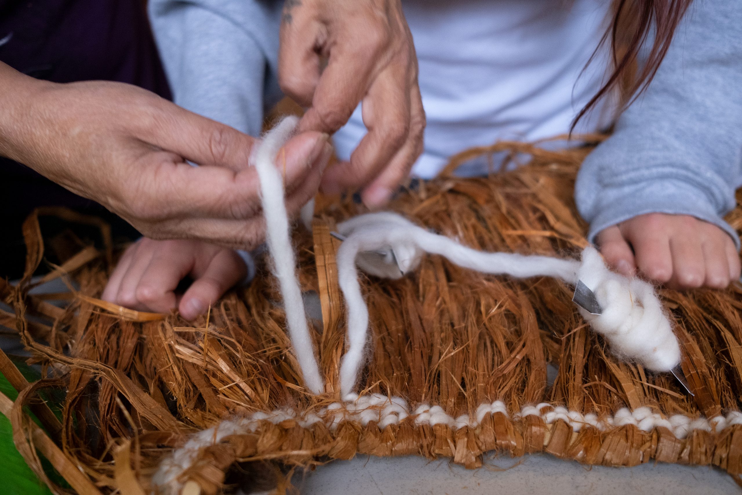 Closeup image of four hands weaving a cedar cape