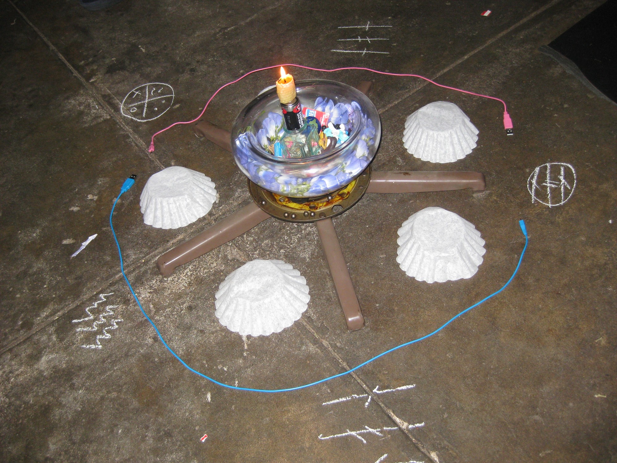 installation of manuel arturo abreu's - upside down coffee filters encircled by headphone cables, on concrete floor with chalk markings around the edits, in center is an object with candle burning